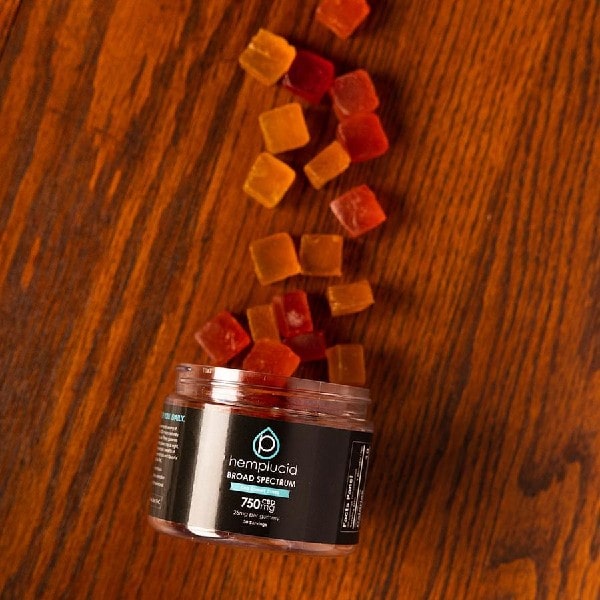 Broad Spectrum CBD Gummy Cubes - THC Free - Hemplucid - Photo of CBD Gummy Jar Tipped Sideways With Gummies Pouring Out On Wood
