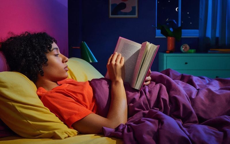 Person reading in a dim bedroom with phone put away as part of a healthy bedtime routine